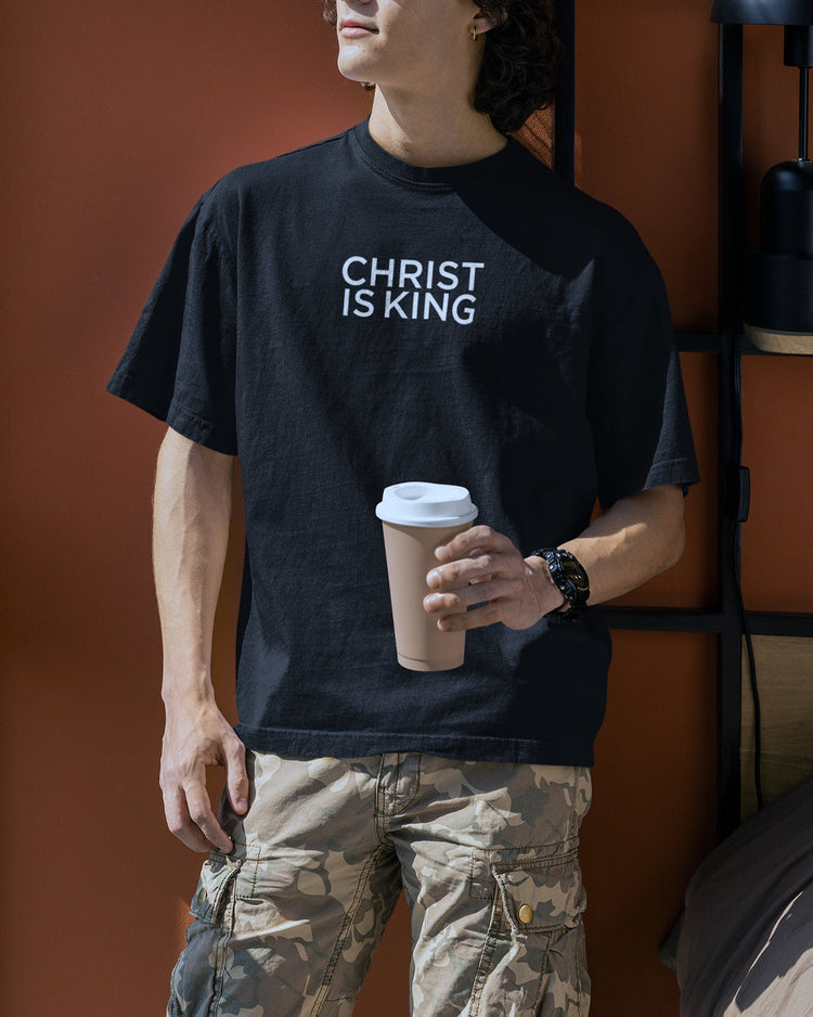 a young man holding a cup of coffee wearing an oversized box t shirt that is black with the words Christ is King