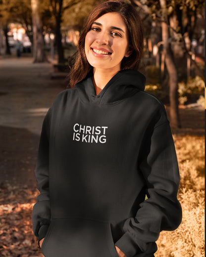 Woman wearing a black christian  hoodie with 'Christ is King' text outdoors.